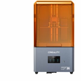 Das Bild zeigt einen HALOT-MAGE 3D-Drucker von Creality. Der 3D-Drucker hat ein dunkelgraues Unterteil mit dem Creality Logo, ein Bedienfeld und den Schriftzug "HALOT-MAGE 8K". Über dem Unterteil ist eine durchsichtige, orangefarbene Kunststoffhaube, durch die man in das Innere des Druckers blicken kann. Der Drucker ist für die additive Fertigung von Objekten mittels 3D-Drucktechnologie konzipiert.