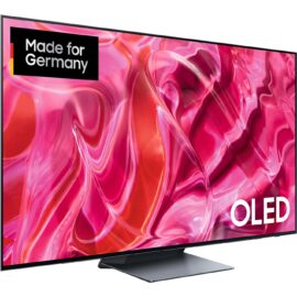 Das Bild zeigt den Samsung OLED-Fernseher GQ-65S92C mit einem lebendigen, abstrakten Hintergrundbild, um die Farbqualität und Bildschärfe des Displays zu betonen. Im Vordergrund ist das Logo "OLED" prominent platziert, während oben rechts im Bild das Zertifikat "Made for Germany" zu erkennen ist, was eine spezielle Anpassung oder Qualität für den deutschen Markt suggerieren könnte. Der Zweck des Bildes ist es, die visuellen Fähigkeiten des Fernsehers hervorzuheben und dessen Design und Eignung für den deutschen Markt zu unterstreichen.
