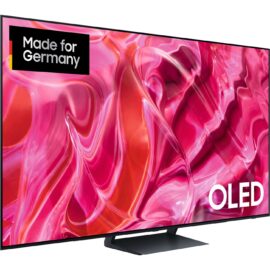 Das Bild zeigt einen Samsung OLED-Fernseher, Modell GQ-77S90C, der ein lebhaftes, farbenfrohes abstraktes Bild anzeigt, das die hohe Bildqualität des Displays hervorhebt. Der Fernseher ist mit dem Schriftzug "OLED" gekennzeichnet und trägt ein Etikett mit der Aufschrift "Made for Germany", was darauf hinweist, dass das Gerät speziell für den deutschen Markt konzipiert wurde. Der Zweck des Bildes ist es, die Qualität und Details der Bildwiedergabe des Fernsehers zu demonstrieren sowie die spezifische Modellbezeichnung für potenzielle Käufer zu bewerben.