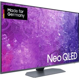 Das Bild zeigt einen Samsung Neo QLED GQ-50QN90C QLED-Fernseher. In der oberen linken Ecke des Bildschirms befindet sich ein Label mit der Aufschrift "Made for Germany", was darauf hindeutet, dass dieses Produkt speziell für den deutschen Markt hergestellt wurde. Der Bildschirm des Fernsehers ist eingeschaltet und zeigt eine lebendige Abbildung mit mehreren lila Nuancen, was die Bildqualität und Farbintensität des QLED-Displays demonstriert. Der Fernseher weist ein schlankes, modernes Design mit schmalen Rändern auf und steht auf einem ebenso minimalistisch gestalteten Standfuß. Der Zweck dieses Bildes ist es, das Produkt in einem werbewirksamen Licht zu präsentieren, indem die visuellen Merkmale und das Design des Fernsehers hervorgehoben werden.
