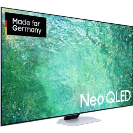 Das Bild zeigt den Neo QLED GQ-55QN85C QLED-Fernseher, der auf einem Standfuß steht. Auf dem Bildschirm ist eine lebendige, hochaufgelöste Darstellung von klarem, türkisfarbenem Wasser zu sehen, die die Bildqualität des Fernsehers hervorheben soll. In der oberen linken Ecke des Bildschirms befindet sich ein Label mit der Aufschrift "Made for Germany", und im unteren rechten Bereich ist prominent der Schriftzug "Neo QLED" platziert. Der Zweck des Bildes ist es, die hohe Bildqualität und das Design des Fernsehers zu veranschaulichen, sowie die Tatsache zu betonen, dass das Produkt für den deutschen Markt konzipiert wurde.